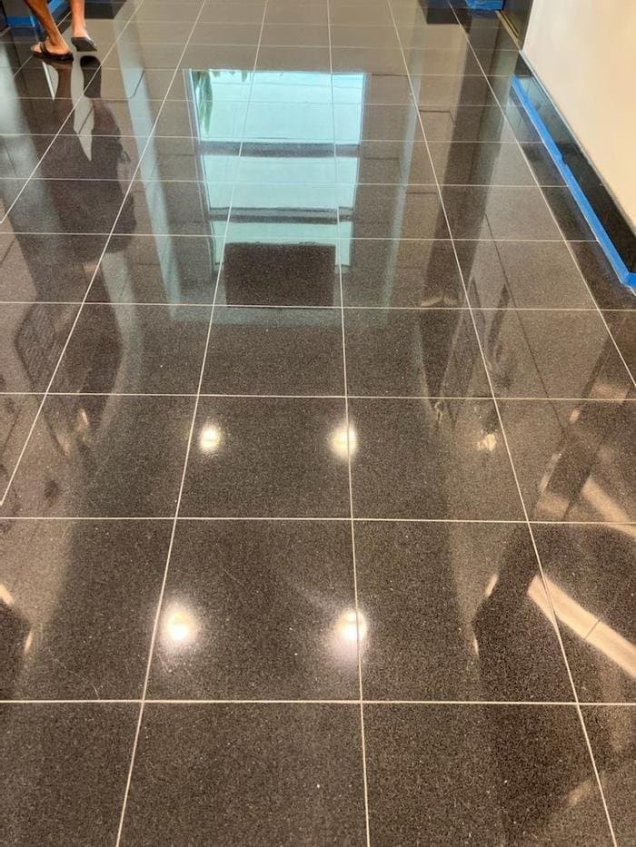 Black polished stone tile floor with thin grout lines and a mirror-like finish, with blue tape along the wall