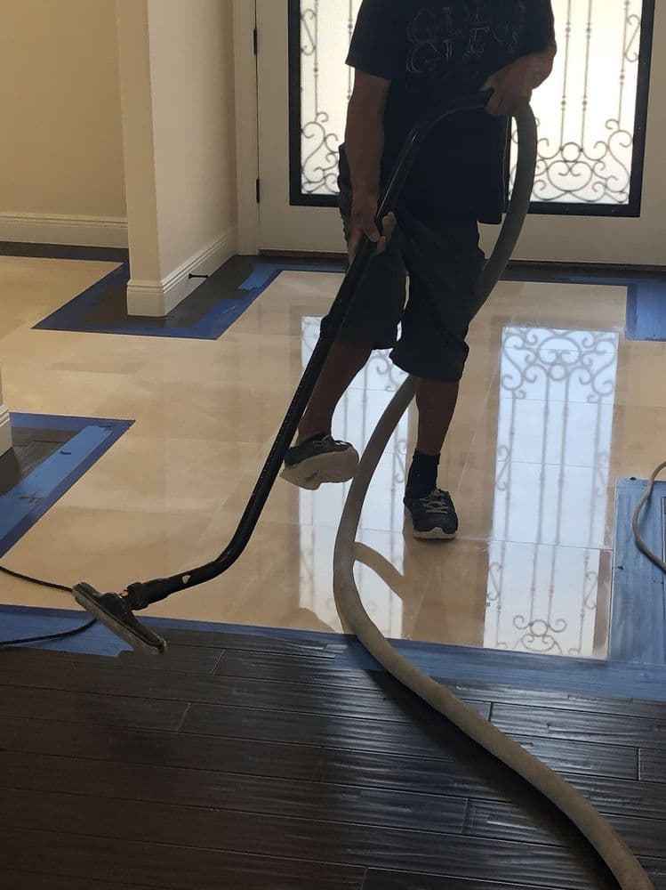 Technician wet-vacuuming a polished cream marble entryway floor with blue tape protecting the hardwood