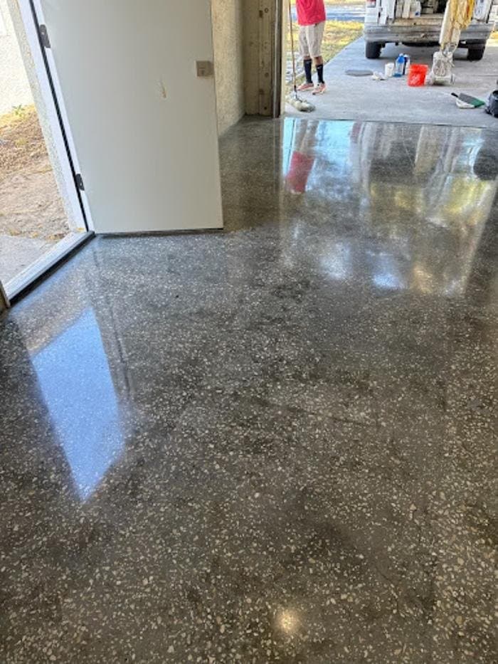 Dark polished concrete floor with exposed aggregate and a glossy reflection of the doorway