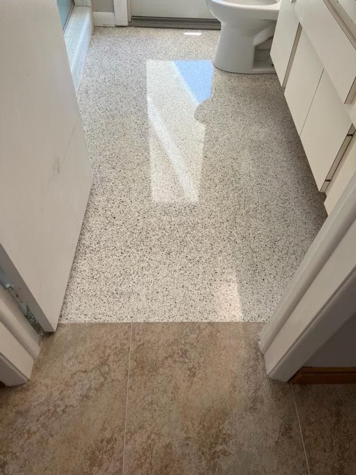 Polished gray and white terrazzo bathroom floor next to beige tile