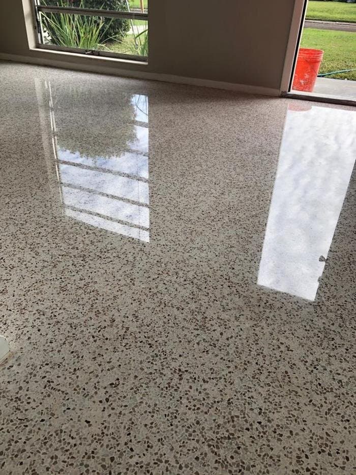 Glossy sealed terrazzo floor with brown and tan chips reflecting windows and a sliding door